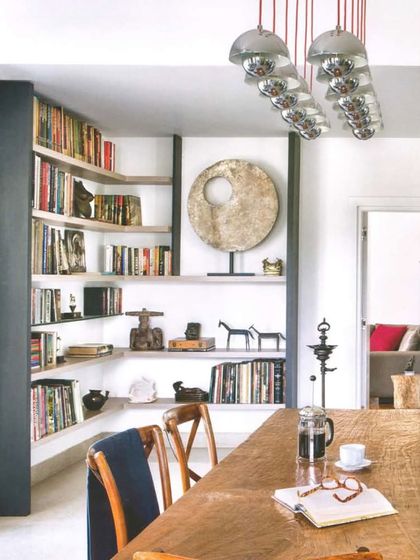 This dining nook from the Aishbagh project, featured in Architectural Digest, showcases a more intimate and eclectic style. Built-in shelves are filled with books and collected objects, creating a personal and lived-in feel around the rustic wooden dining table.