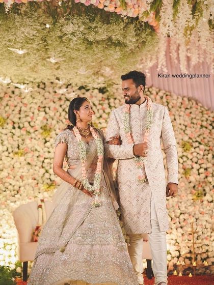 A romantic shot of a couple on their reception stage, which is covered in a mountain of white flowers and topped with hanging floral chandeliers.