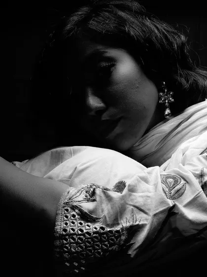 A low-key black and white shot where the model is curled up in shadow. The image focuses on form and emotion, using darkness to create a contemplative and artistic mood.