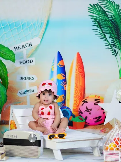 A full view of our beach setup for a "Halfway to One" shoot. The baby girl sits on a beach chair with a chalkboard sign, surfboards, and sand.