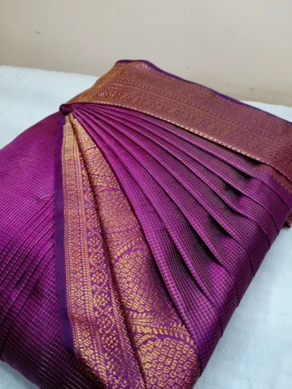 A deep purple silk saree with a rich gold border, ready for a wedding or festive event.