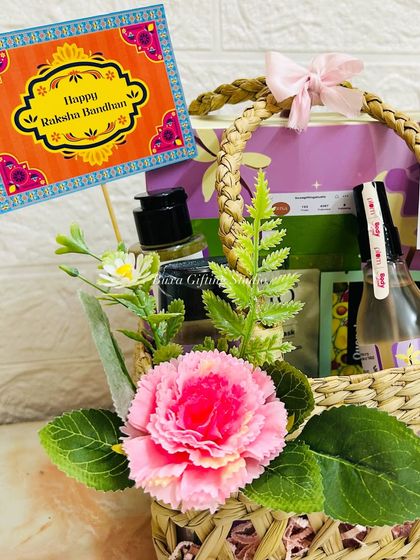 A close-up of the Rakhi hamper for a sister, showing the mesh jute basket, pink floral decorations, and a "Happy Raksha Bandhan" card.