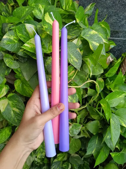 A trio of taper candles in pastel shades of lavender, pink, and purple.