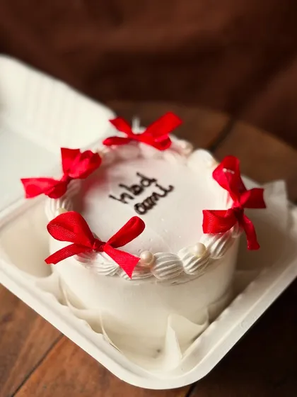 A classic white bento cake decorated with red ribbon bows and pearl sprinkles for a birthday.