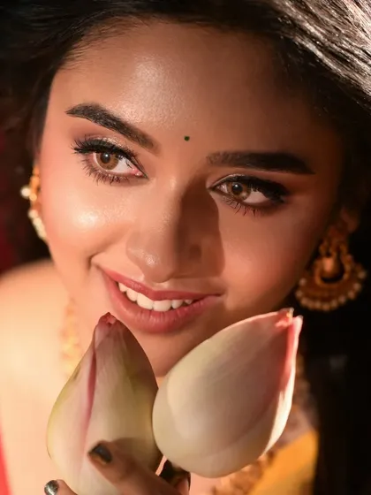 A close-up portrait of a model holding lotus buds. The soft lighting and her gentle smile create a serene and beautiful image, highlighting her natural beauty and the traditional accessories.
