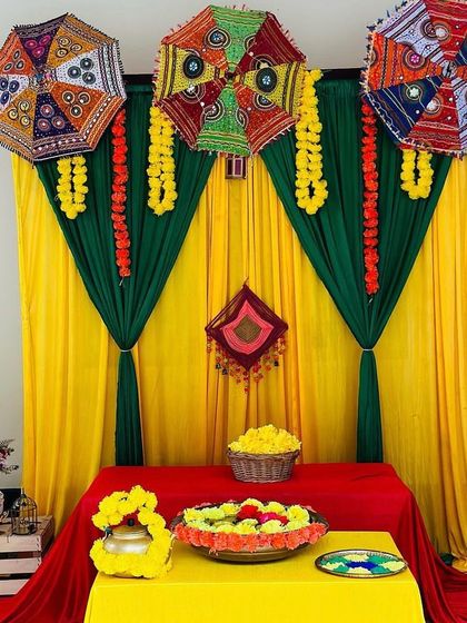 A closer look at a traditional Mehendi decor setup. This highlights the details of the mirror-work Rajasthani umbrellas, marigold garlands, and the colorful draped backdrop, perfect for smaller home functions.