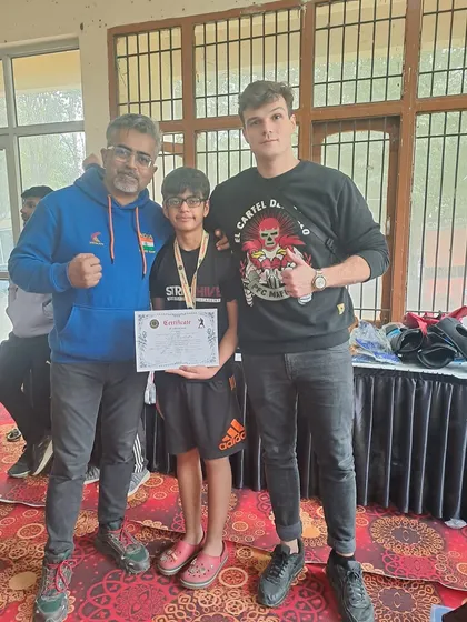 A young competitor receives his medal and certificate, flanked by his proud coaches.