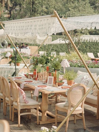 A long dining table set for a poolside brunch, with custom-printed canopies providing shade and style.