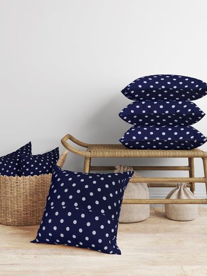 A lifestyle shot of our navy polka dot cushions, stacked and placed in a cozy room setting. This shows the product in a realistic environment, boosting its appeal.