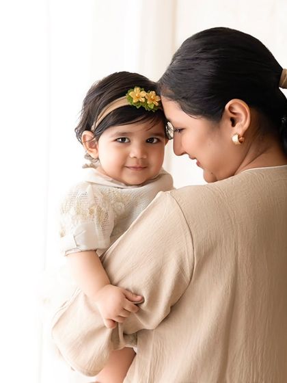 A mother and her baby share a gentle moment, touching foreheads in a softly lit, tender portrait.