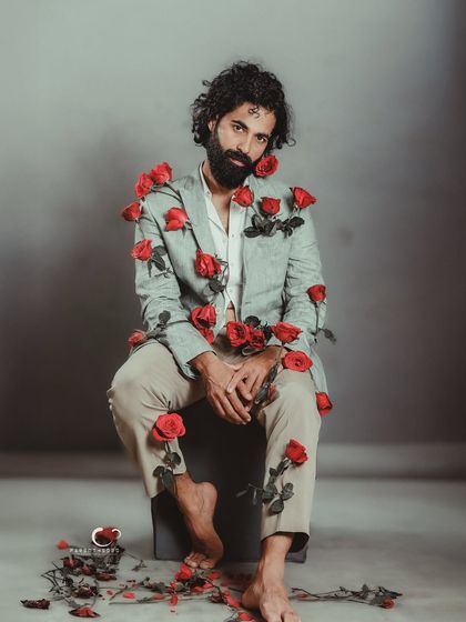 A direct and engaging portrait, challenging the viewer to interpret the story. The contrast between the formal suit and the scattered roses is visually striking.