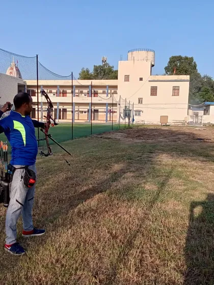 An archer viewed from the side, showing the alignment and focus required to shoot accurately. The spacious field provides a safe environment for practice.