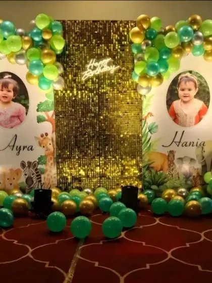 A jungle-themed first birthday for twins, featuring personalized photo backdrops, a central sequin panel, and green and gold balloon arches.