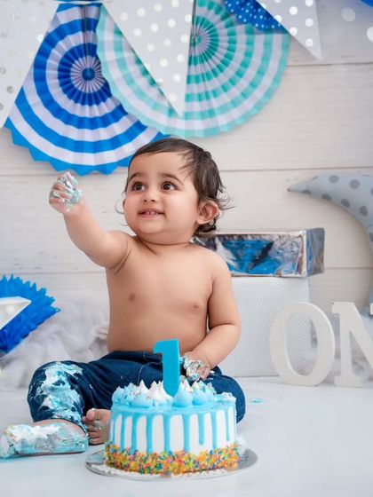 Holding up a hand full of frosting, this little guy is a natural at his first cake smash. These are the fun, messy memories we love to create.