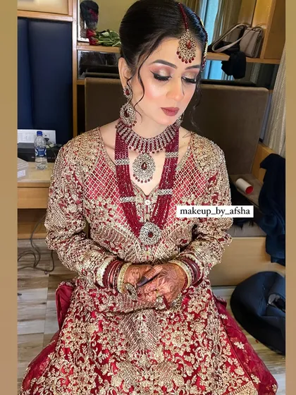 A close-up of this bride's beautiful makeup. The focus is on her eyes, with a dramatic winged liner and soft shimmer, paired with a nude lip to balance her heavy red jewellery.