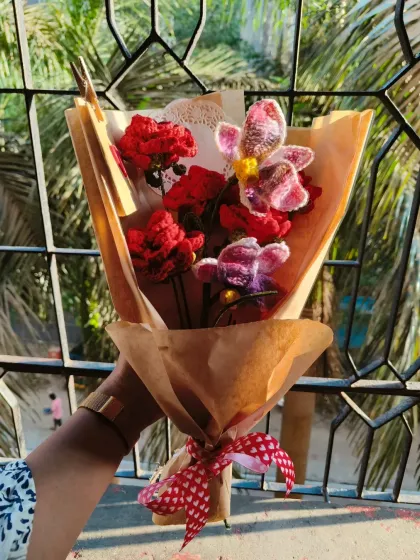 A beautiful combination of deep red roses and delicate crochet orchids. This bouquet has a rustic feel with the brown paper wrapping and heart-patterned ribbon.