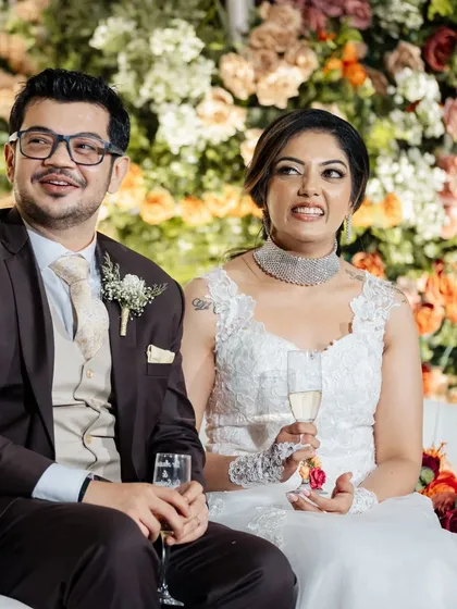 The happy couple enjoying their wedding reception. The lush, multi-colored floral wall behind them adds a vibrant and celebratory feel to their candid photos.
