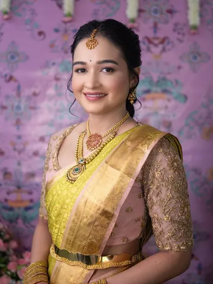 A bride looking lovely in a lime green and pink Kanchipuram saree. Her custom pink blouse features delicate gold embroidery on sheer sleeves for a modern touch.