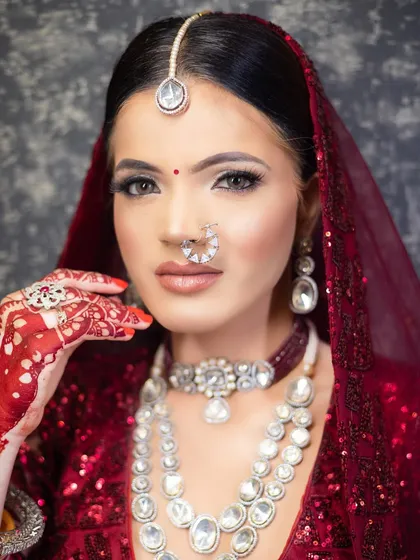 A classic bridal portrait showing the intricate details of the makeup and henna. The look features defined eyes, a neutral lip, and flawless skin, paired with stunning diamond jewelry.