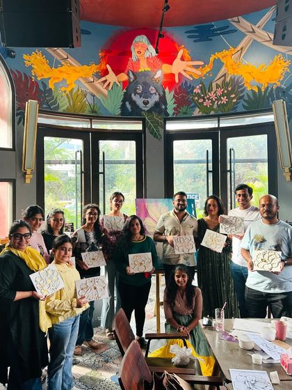 A group of beginner artists proudly holding their finished texture art pieces in a beautifully decorated cafe.