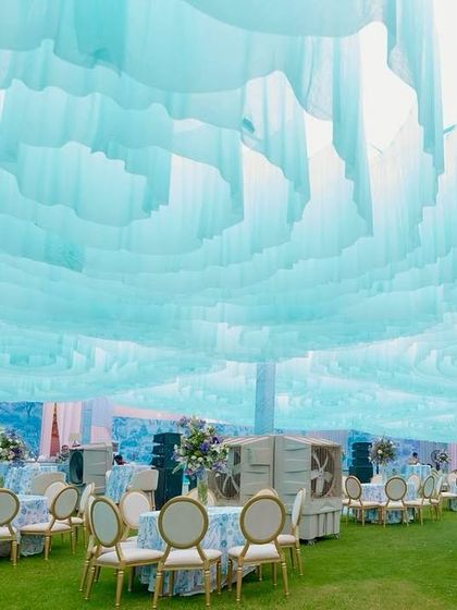 The entire space was transformed with a dreamy, cloud-like ceiling made of flowing pastel blue fabric. This overhead installation complements the Dior-inspired theme and creates a soft, ethereal ambiance for the daytime event.