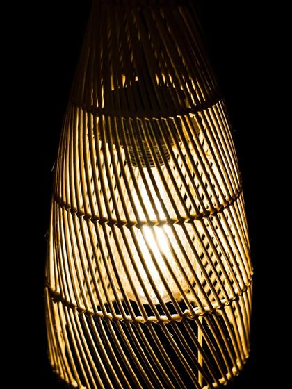An up-close view of the conical lamp's weave. The light catches the natural texture of the bamboo, showcasing the material's inherent beauty and the skill involved in its construction.