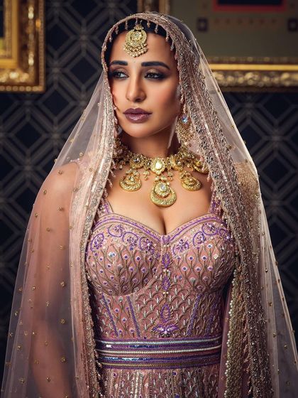 A regal bridal portrait featuring a heavily embroidered lehenga and a sheer veil. The lighting and pose are designed to convey a sense of majesty and grace, suitable for high-end bridal campaigns.
