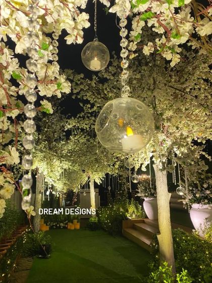 A magical pathway through an enchanted garden I designed. The walkway is lined with white blossom trees, with hanging glass baubles containing LED candles that create a soft, romantic glow.