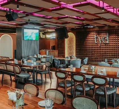 This wide shot shows the main dining floor with its mix of seating options, from banquettes to freestanding tables. The acoustic panels on the ceiling are arranged in a geometric pattern, adding visual interest while managing the sound in the large, open space.