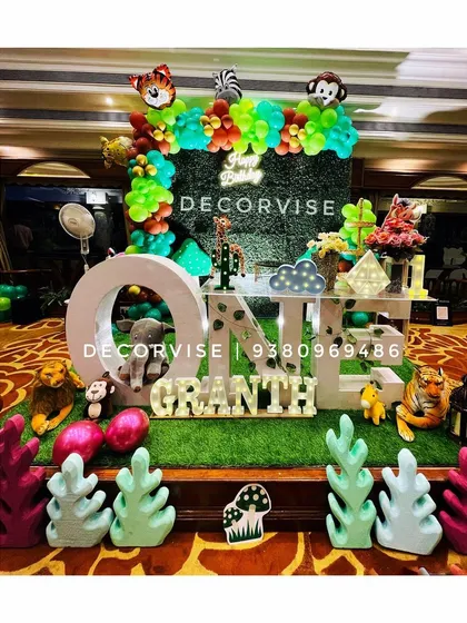 We bring the jungle to your party with our "Wild One" safari theme. This immersive setup for Granth's first birthday features a lush green backdrop, large "ONE" lettering, character cutouts of jungle animals, and themed props to create an exciting adventure for your little explorer.
