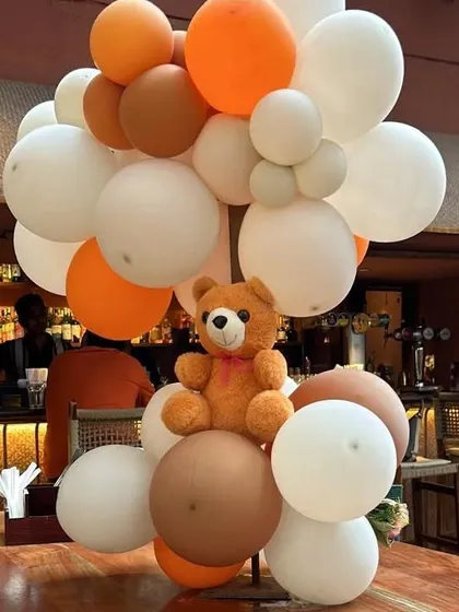 A cute teddy bear centerpiece surrounded by balloons in fall shades, perfectly matching the 'Little Cutie' theme.