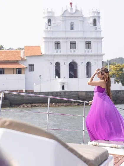 A grand shot featuring the couple on a yacht with a beautiful white Goan church in the background, combining luxury with local charm.