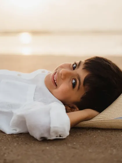 A young boy lies on the sand, smiling contentedly after a day of play. A peaceful and beautiful portrait from a family beach session.