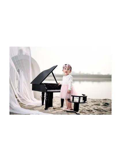 Standing proudly by her instrument. This little girl is ready to play, creating a confident and adorable portrait at her beachside piano recital.
