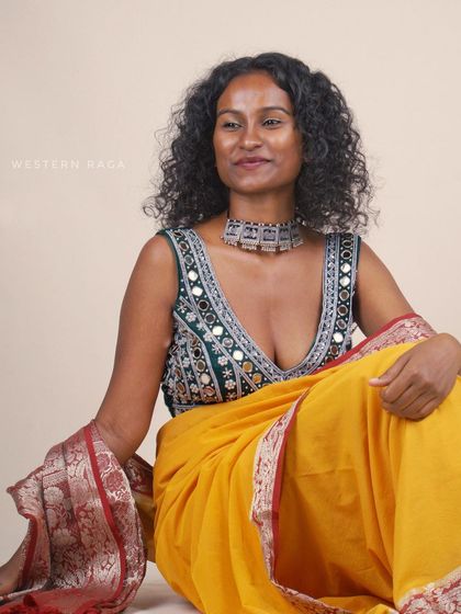 A seated portrait of the model in the green Shisha blouse and yellow saree. This composed shot highlights both the product and a serene, elegant mood.