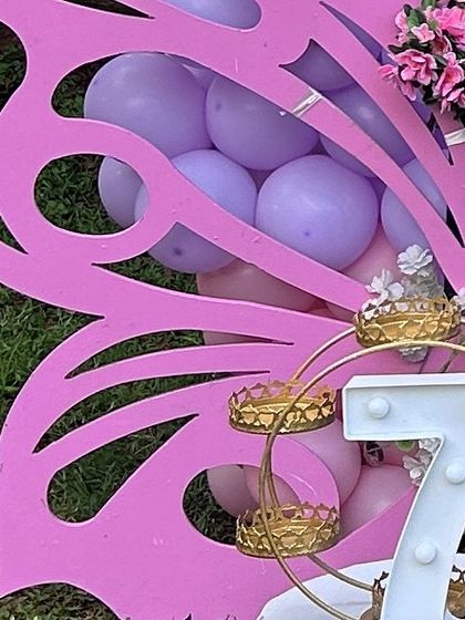 A close-up of a large pink butterfly wing prop. This piece is perfect for photo opportunities and adds a bold, thematic element to the decor, shown here next to a light-up number '7'.