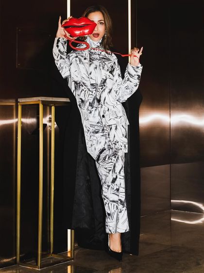 A full-length version of the playful portrait with the lip-shaped phone, showing off the complete look from head to toe.