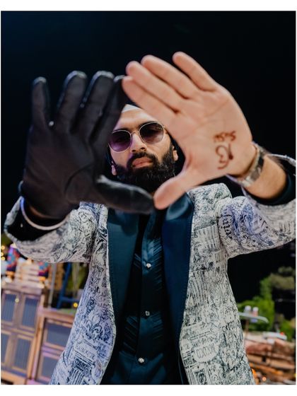 A creative portrait of the groom, framing his face with his hands, one of which shows his bride's name in henna.