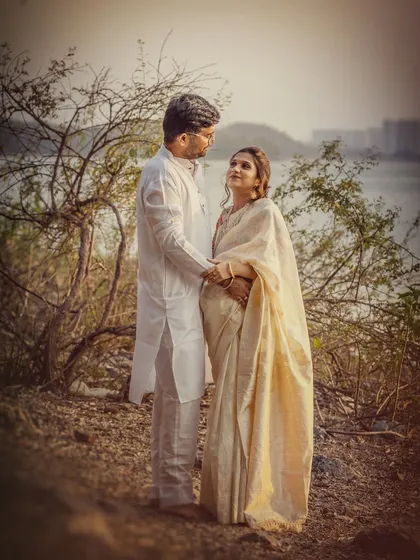 A full-length shot of the couple by the river, capturing the elegance of the cream-coloured saree against the rustic, natural setting. Their pose feels both classic and candid.
