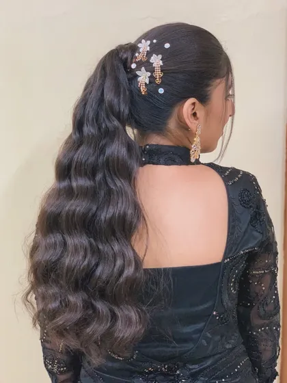 A view of this stunning retro-inspired wavy ponytail from the back. The addition of delicate floral accessories adds a touch of elegance to this chic and modern party hairstyle.