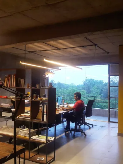 Our architecture studio in Ghitorni, designed as an open, collaborative environment. The space combines raw concrete ceilings, a feature yellow wall, and a large window framing the green landscape.