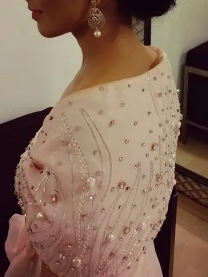 A closer look at the delicate hand embroidery on the pink gown. Each pearl and sequin is carefully placed to create a soft, dreamy effect on the off-shoulder cape.