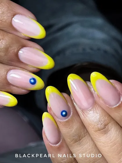 A playful and trendy design featuring bright yellow French tips with an evil eye accent. This look combines a classic technique with a modern, symbolic art piece for a fun and protective vibe.