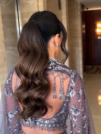 A chic and modern high ponytail with soft, flowing waves. This style is perfect for keeping hair off the face while still showing off its length and volume, making it a great choice for a Sangeet or reception.