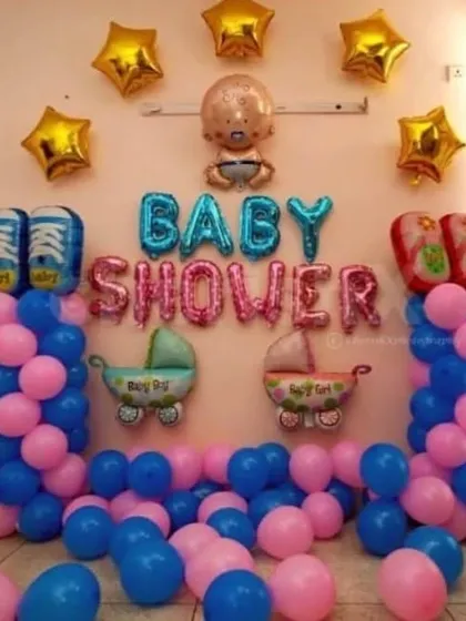 A classic pink and blue baby shower decoration. The setup includes 'Baby Shower' foil letters, balloon columns, and cute props like baby carriage and shoe foil balloons.