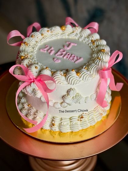 The full view of the "Oh Baby" vintage cake, showcasing the intricate piping and delicate pink ribbon bows.