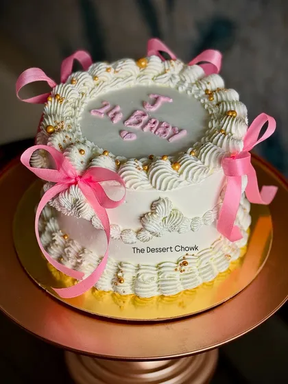 A beautiful vintage-inspired tall cake with intricate white piping and pretty pink ribbons.
