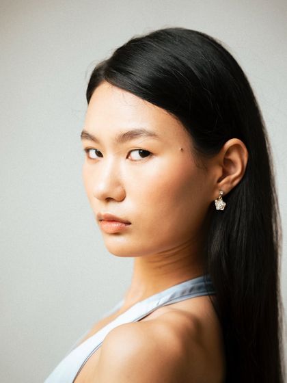 A clean and direct beauty-focused headshot. The simple lighting and neutral background ensure the focus remains on the model's natural features and the delicate earring, perfect for an editorial or lookbook.
