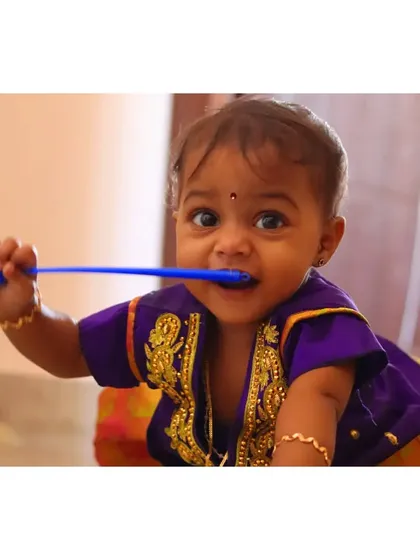 A fun and candid shot of a baby girl in a traditional purple outfit, playfully chewing on a toy. It's these real, everyday moments that often make the best pictures.