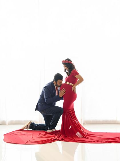 A tender moment as the dad-to-be kisses the baby bump. The clean white background makes the couple and the beautiful red gown the complete focus of the image.